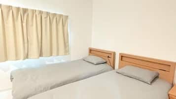 A room with two beds, a window with curtains, and a wooden headboard.