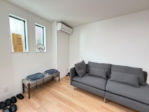 A modern living room with a grey sofa, a bench with cushions, and two windows with artwork. - Ichizuru House Tsuruhashi OSAKA (Osaka)