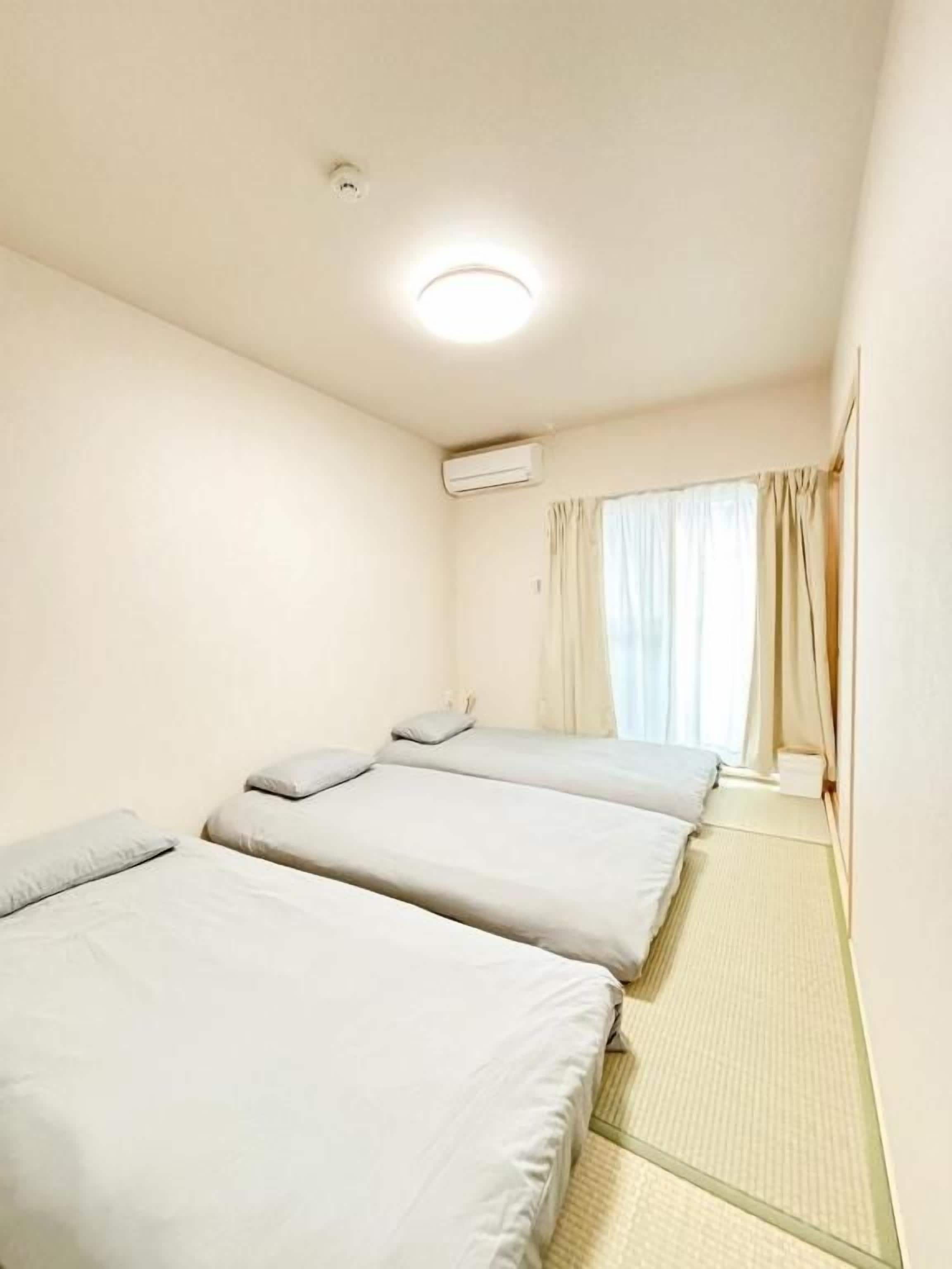 A hotel room with two beds, a ceiling light, an air conditioning unit, and a window with curtains.