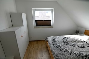 Un dormitorio con techo inclinado, una ventana con persianas, una cama con colcha estampada y un armario.