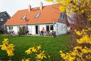 A house with a red-tiled roof, a covered patio, and a lawn with yellow flowers. - Crane view - happiness (Groß Schwansee)
