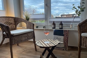 A room with wicker furniture, a small wooden table, and bottles on a windowsill. - Crane view - happiness (Groß Schwansee)