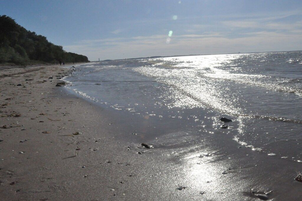 A beach with a clear sky, calm sea, and a distant shoreline.