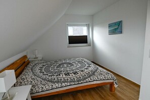 Quarto com cama, janela, um quadro e uma pequena mesa.