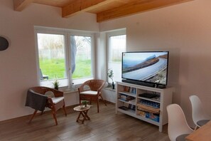 Una sala de estar con televisión, dos sillones de mimbre, una mesita y una estantería.