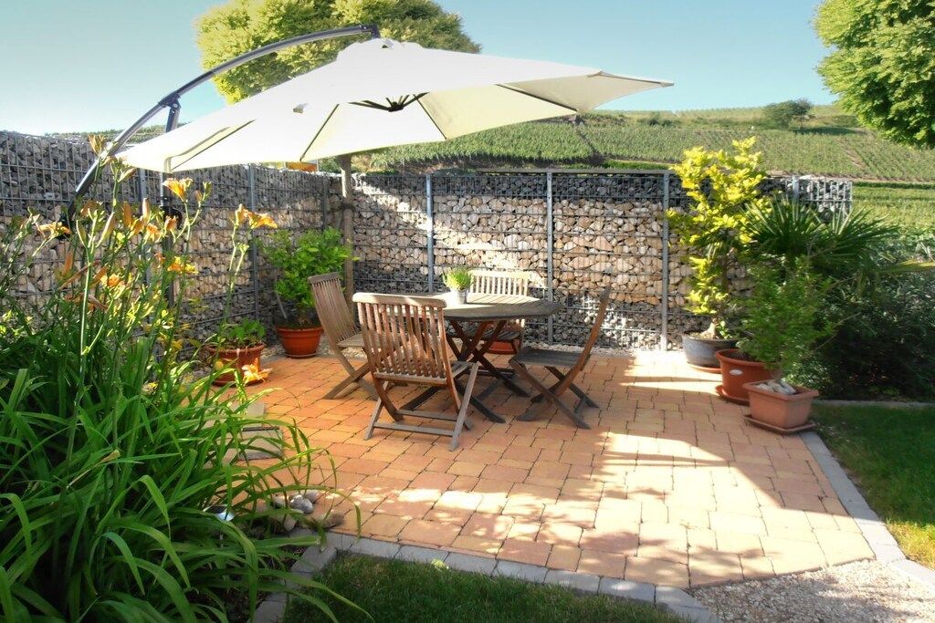 An outdoor patio with a table and chairs, surrounded by potted plants and a stone wall.