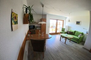 A living room with a dining table, chairs, a green sofa, and a plant. - Patricias House; Apartment Henkenberg (Vogtsburg)