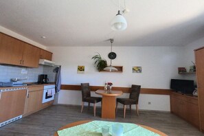 A compact kitchen with a dining area, wooden cabinets, a coffee machine, and a television. - Patricias House; Apartment Henkenberg (Vogtsburg)