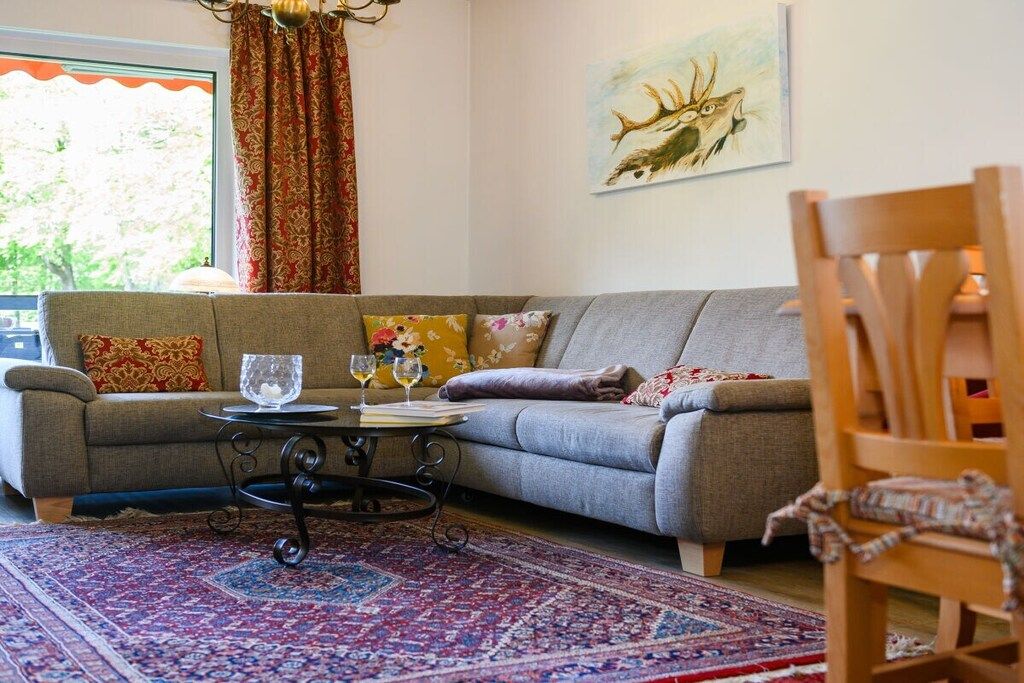 Een woonkamer met een grijze bank, gekleurde kussens, een bijzettafeltje met glazen, een vloerkleed en een schilderij van een hert op de muur.