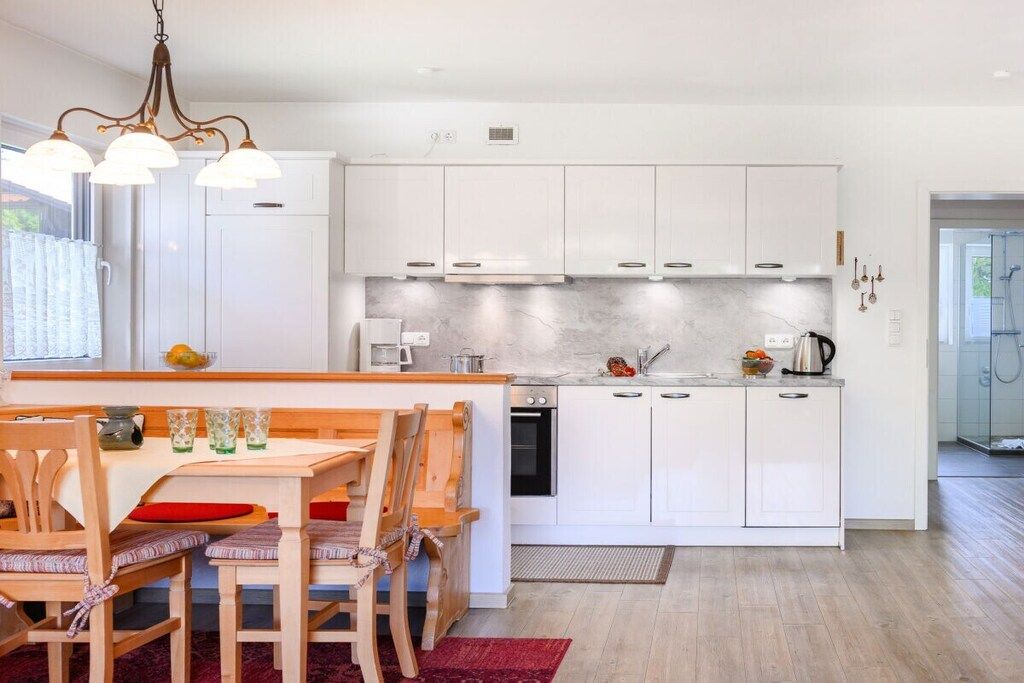 Eine moderne Küche mit weißen Schränken, einer zentralen Kochinsel und einem Essbereich mit Holzkästen und einem roten Teppich.