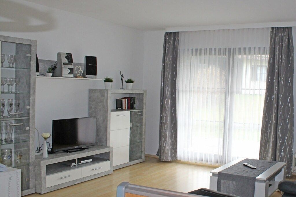 En moderne stue med et fladskærms-tv, indbyggede reoler, et sofabord og et stort vindue med lette gardiner.