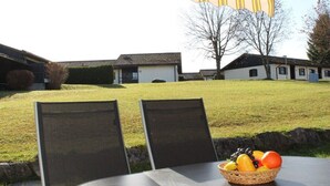 Área externa com mesa e cadeiras, uma cesta de frutas e vista para edifícios residenciais ao fundo.