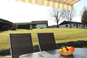An outdoor seating area with a table and chairs, a basket of fruit, and a view of residential buildings in the background. - Holiday home Aggenstein (Lechbruck)