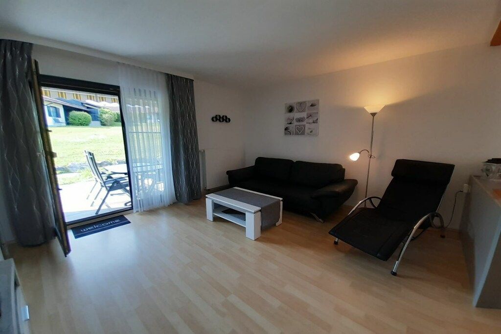 Ein Wohnzimmer mit einer Couch, einem Couchtisch, einem Sessel, einer Lampe und einer Tür zum Balkon.