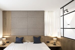 Ein Hotelzimmer mit einem großen Bett, zwei Nachttischen, einem Kopfteil mit strukturierter Wandverkleidung und einem Fenster mit Vorhängen.