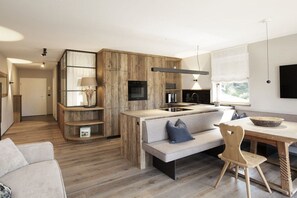 Eine moderne Küche mit Holzschränken, einem Einbauofen und einem Essbereich mit einer Bank und einem Tisch.