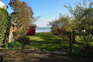 A paved pathway leading to a red structure with a view of a body of water. - Holiday home in Fehmarn with swimming pool (Fehmarn)