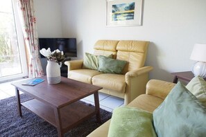 A living room with a sofa, a coffee table, a television, and a window with curtains. - Holiday home in Fehmarn with swimming pool (Fehmarn)