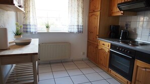 A kitchen with wooden cabinets, a stove, and a window with curtains. - Holiday home in Fehmarn with swimming pool (Fehmarn)