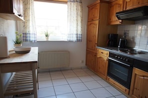 A kitchen with wooden cabinets, a stove, and a window with curtains. - Holiday home in Fehmarn with swimming pool (Fehmarn)