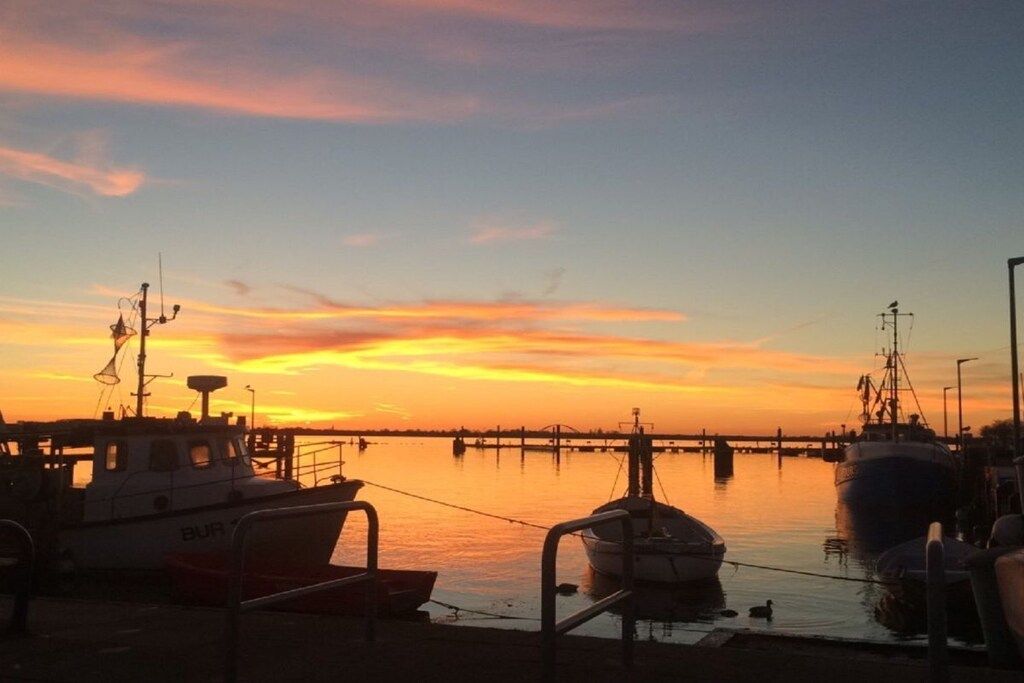 Un port de plaisance avec des bateaux amarrés, une jetée s’avançant dans l’eau et un coucher de soleil en arrière-plan.