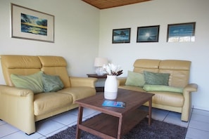A living room with two beige sofas, a coffee table, and three framed pictures on the wall. - Holiday home in Fehmarn with swimming pool (Fehmarn)