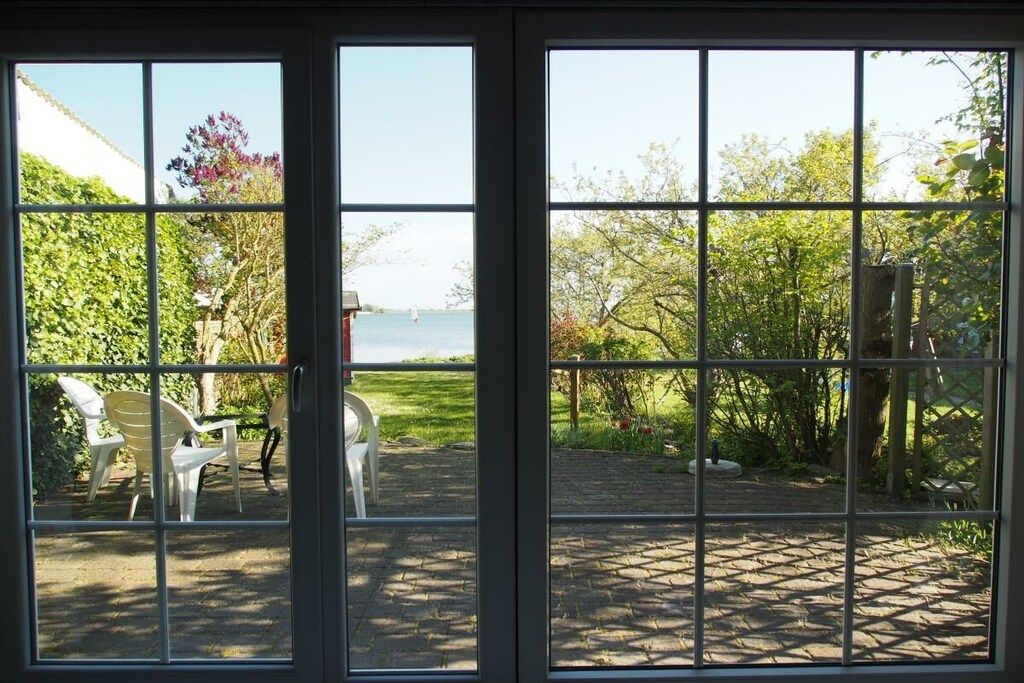 A view through a window with a garden and a body of water visible outside.
