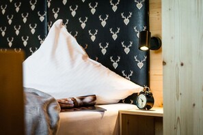 A cozy room with a bed, a pillow, a book, a wall clock, and a patterned wallpaper. - Holiday apartment with 1 bedroom (Garmisch-Partenkirchen)