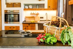 Une cuisine équipée d’une cuisinière, d’un four et d’un panier rempli de produits frais posé sur le plan de travail.