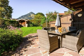 Eine Terrasse im Freien mit Korbmöbeln, einem Glastisch und Blick auf Berge.