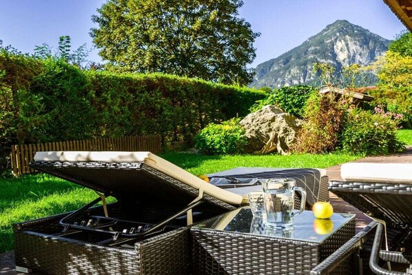 Een terras met rieten meubilair en een glazen tafel, met op de achtergrond weelderige begroeiing en een berg.