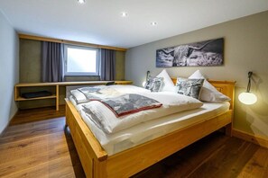 Een slaapkamer met een houten bed, een bureau, een raam met gordijnen en een wandlamp.