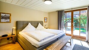 A bedroom with a bed, bedside tables, a bench, a window with curtains, and a view of greenery outside. - Holiday apartment with 2 bedrooms (Farchant)