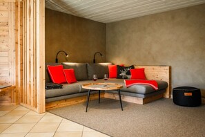 Une pièce chaleureuse avec un banc en bois, un canapé avec des coussins rouges, une petite table ronde et un pouf noir.