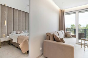 A modern bedroom with a bed, bedside table, and a view of the outdoors through a large window. - Comfortable Apartment with a Balcony | Air Conditioning (Gdańsk)