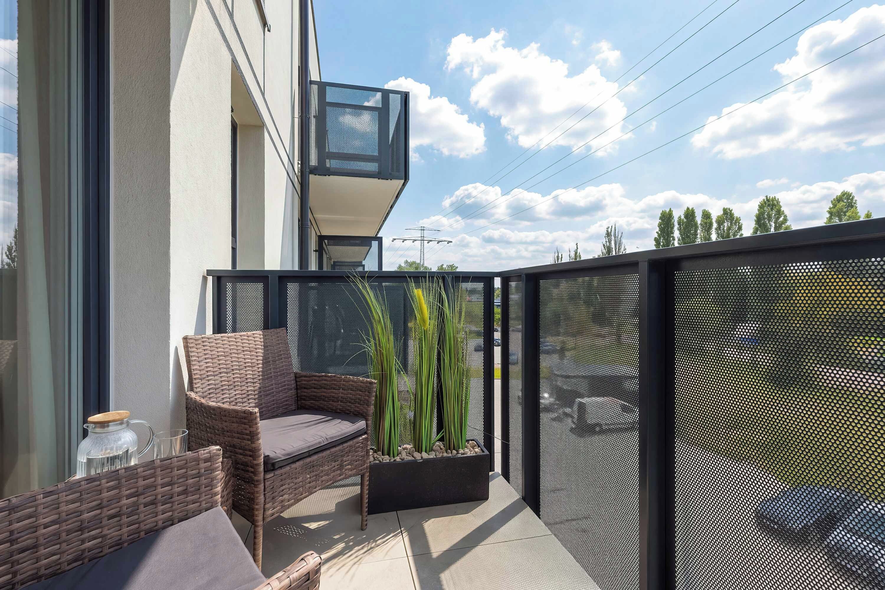 A balcony with wicker furniture, a planter with tall plants, and a modern building facade.
