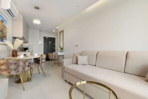 A modern living room with a sofa, a dining area with chairs, and a kitchen in the background. - Comfortable Apartment with a Balcony | Air Conditioning (Gdańsk)