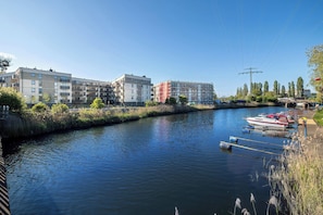 A river with a dock and boats, surrounded by modern buildings and greenery. - Comfortable Apartment with a Balcony | Air Conditioning (Gdańsk)
