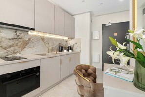 A modern kitchen with a marble backsplash, stainless steel appliances, and a unique chair with a gold frame. - Comfortable Apartment with a Balcony | Air Conditioning (Gdańsk)