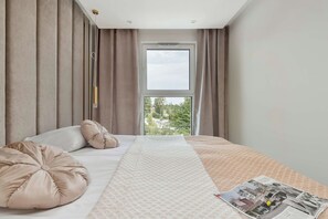 A bedroom with a large bed, a window with a view of trees, and a ceiling light. - Comfortable Apartment with a Balcony | Air Conditioning (Gdańsk)