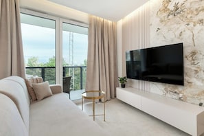 A modern living room with a sofa, a TV mounted on a marble wall, and a balcony with curtains. - Comfortable Apartment with a Balcony | Air Conditioning (Gdańsk)