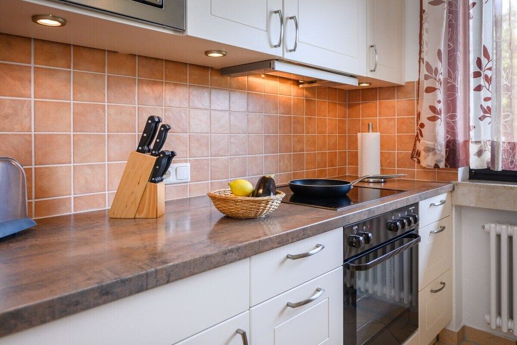 Una cucina con mobili bianchi, un fornello e un piano di lavoro con un portachiodi e una cesta di frutta.