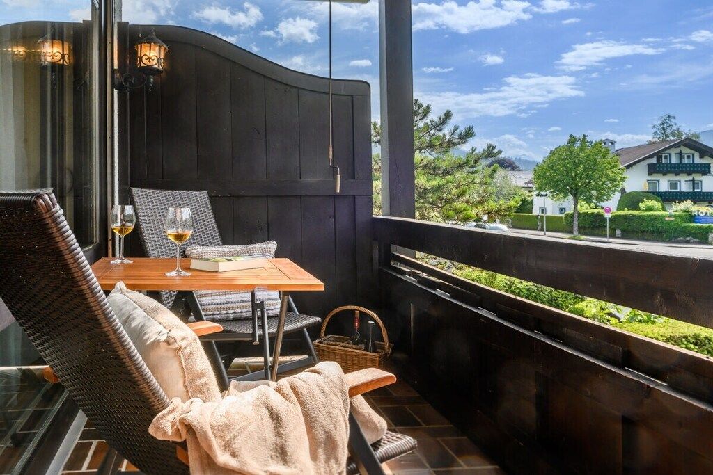 A balcony with wicker chairs, a table with glasses, and a view of the surrounding area.