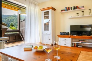 A room with a wooden table, two glasses of wine, a bowl of fruit, a television, and bookshelves. - Holiday apartment with 1 bedroom (Garmisch-Partenkirchen)
