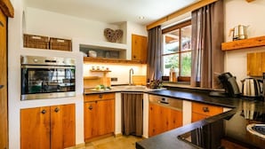 Una cocina moderna con armarios de madera, horno empotrado, lavavajillas y un amplio ventanal con cortinas.