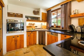 Een moderne keuken met houten kastjes, een inbouwoven, een vaatwasser en een groot raam met gordijnen.