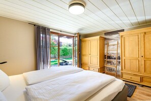 Une chambre à coucher avec un lit, une armoire en bois et une vue sur un jardin, accessible par une porte coulissante.