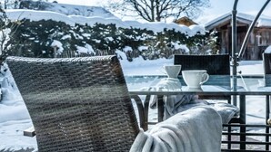 A glass table with two white cups and a wicker chair in a snowy outdoor setting. - Holiday apartment with 1 bedroom (Farchant)