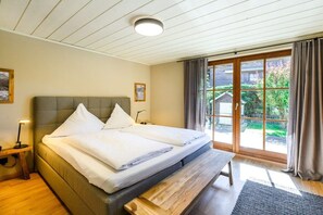 Ein Doppelbett mit Sitzbank, ein Nachttisch und Blick auf einen Garten durch eine Schiebetür.