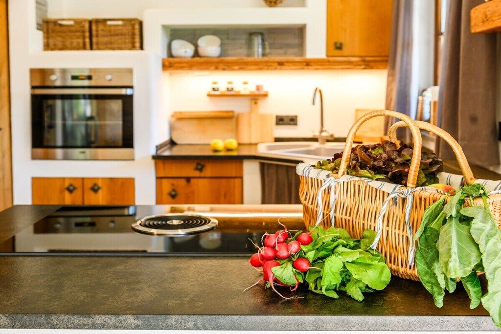 Une cuisine équipée d’une cuisinière, d’un four et d’un panier rempli de produits frais posé sur le plan de travail.